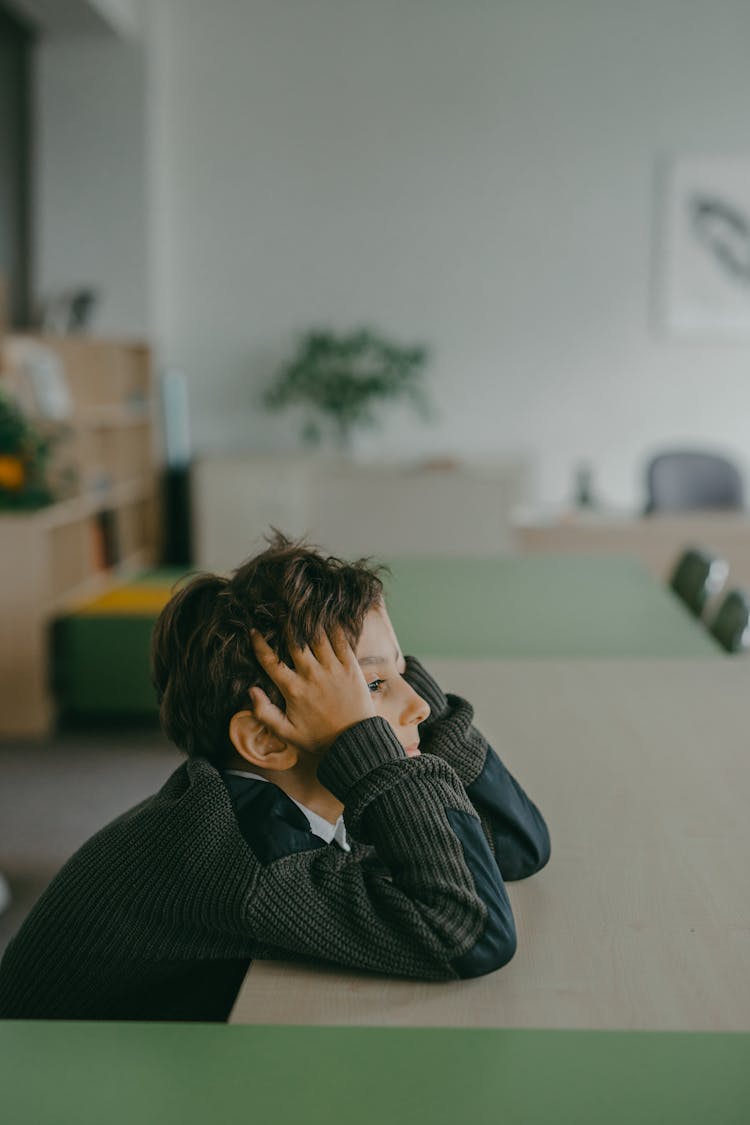 A Boy In A Sweater Leaning On A Table