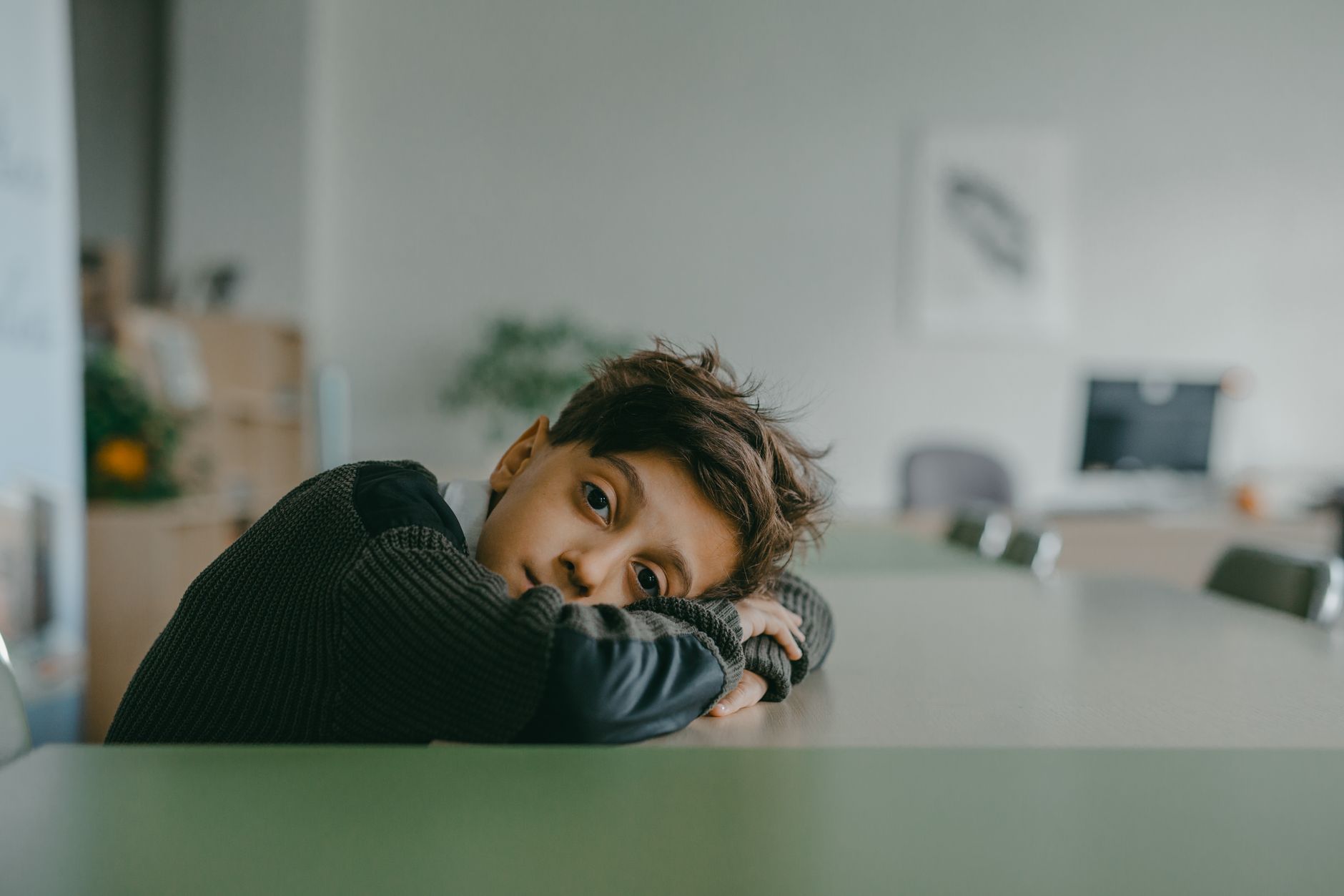 Enfant pensif posant la tête sur un bureau de classe, illustrant le poids invisible de la charge neurocognitive dans un cadre scolaire