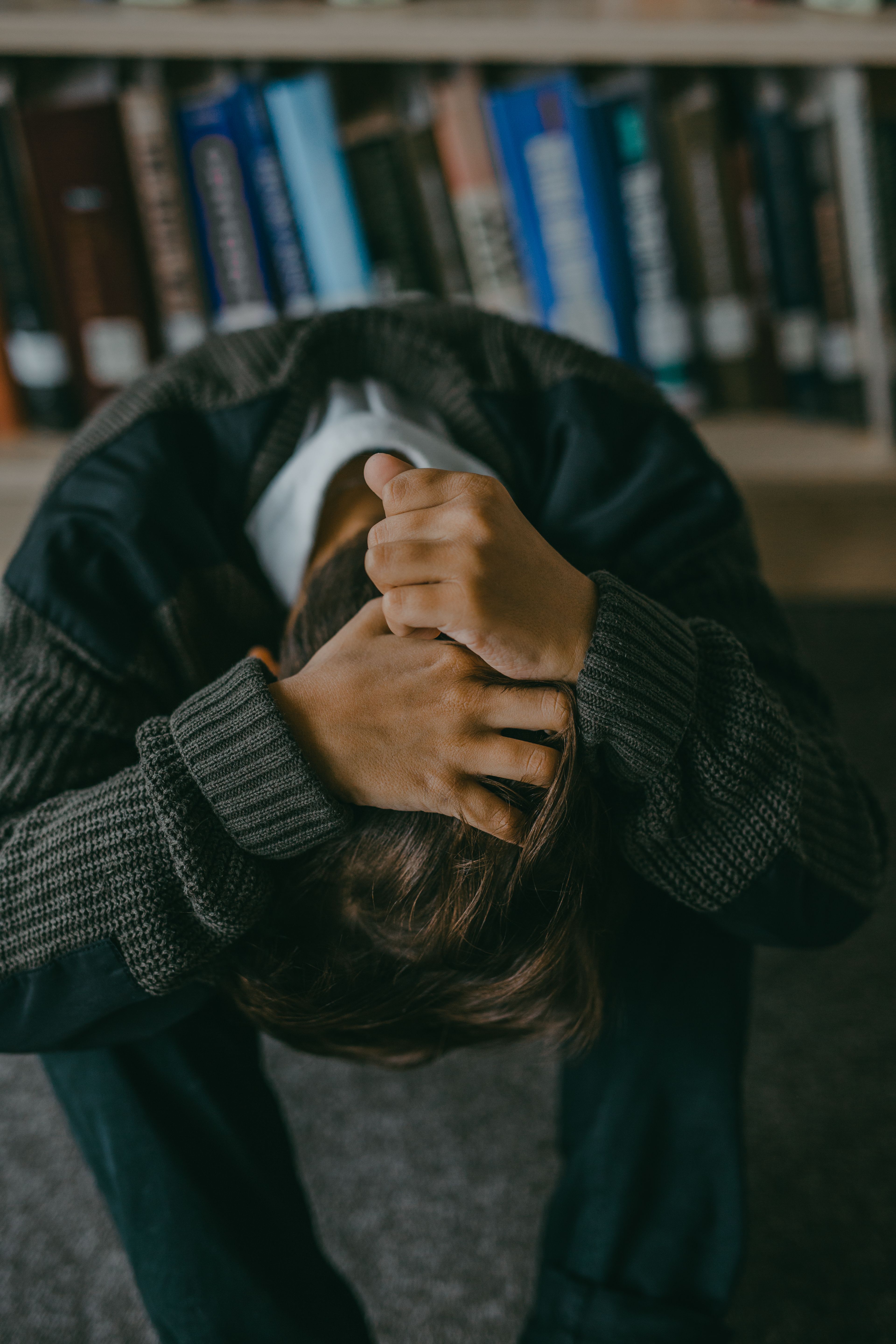 Person sitting with head down and hands on head in a library setting.
