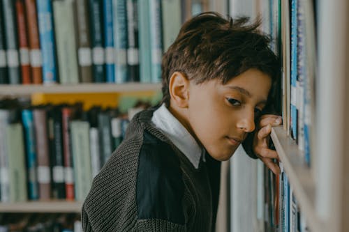 Photo of a Boy Leaning against Bookshelves