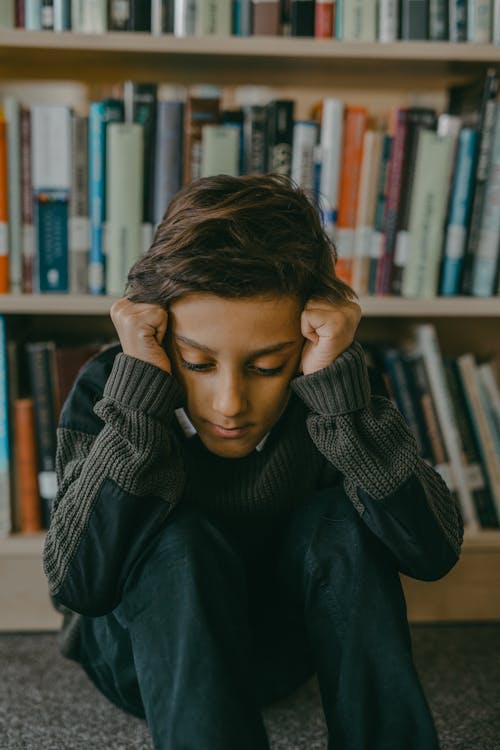 A Stressed Boy Sitting on the Floor of a Library