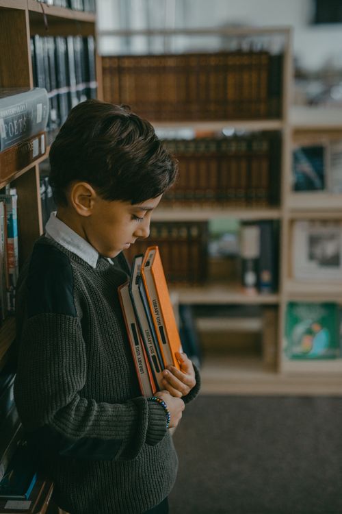 Free A young boy stands thoughtfully in a library, holding books. Education and solitude concept. Stock Photo