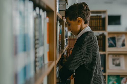 A Boy Grasping Books Inside the Library
