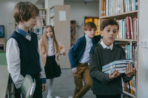Free A group of children interacting in a library setting, focusing on a boy holding books. Stock Photo