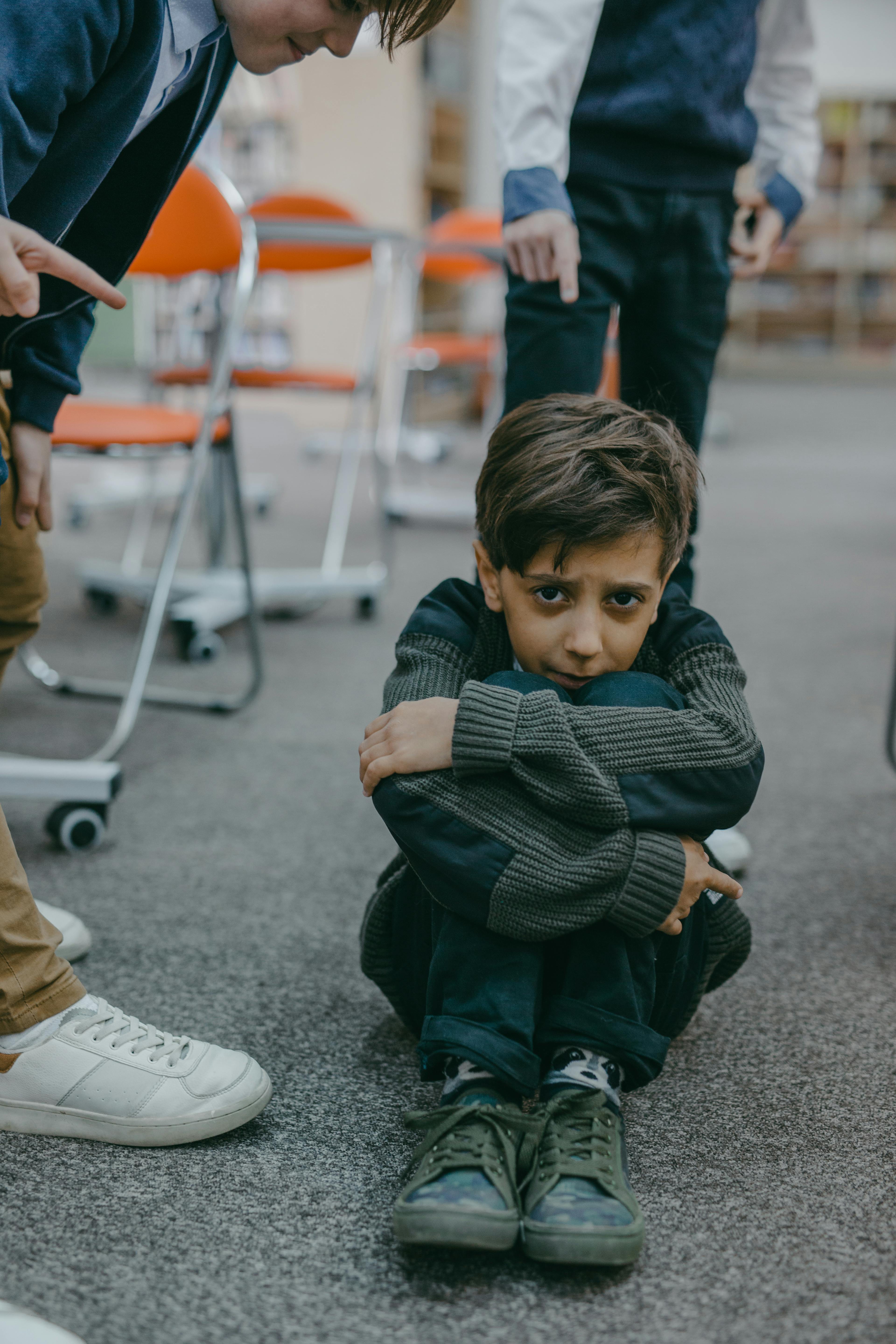 a sad boy sitting on a floor of a classroom