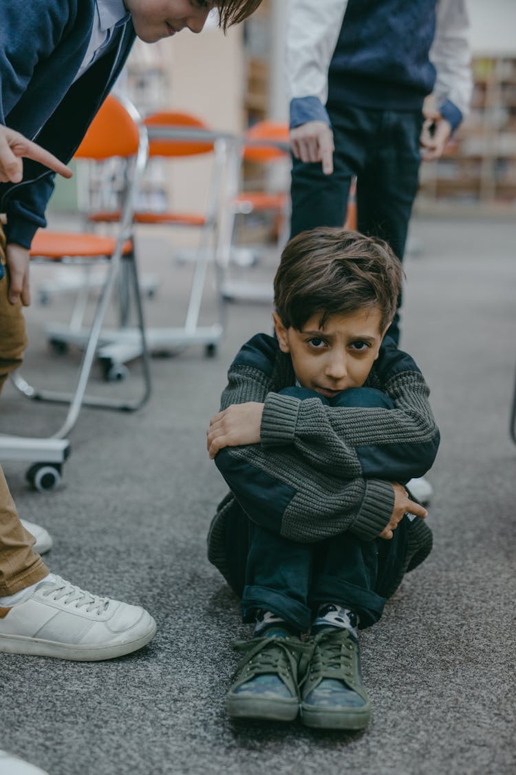 A Sad Boy Sitting On A Floor Of A Classroom