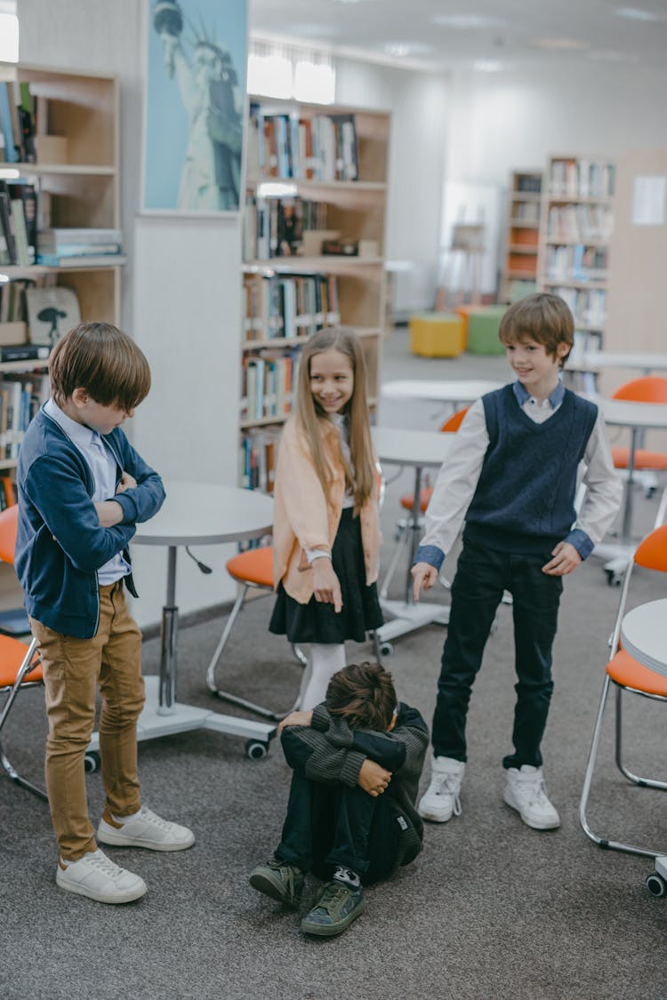 Children Laughing And Bullying A Boy In Gray Sweater Sitting On A Ground 