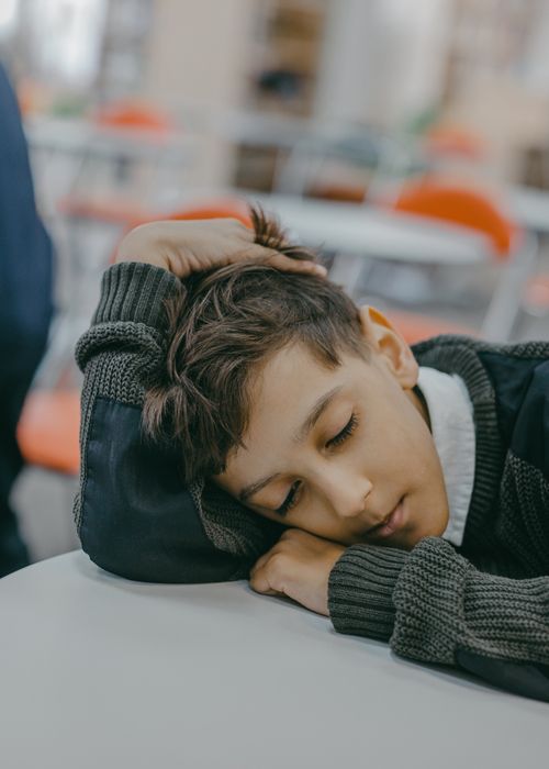 Free A child peacefully sleeping on a desk in a classroom with blurred background. Stock Photo