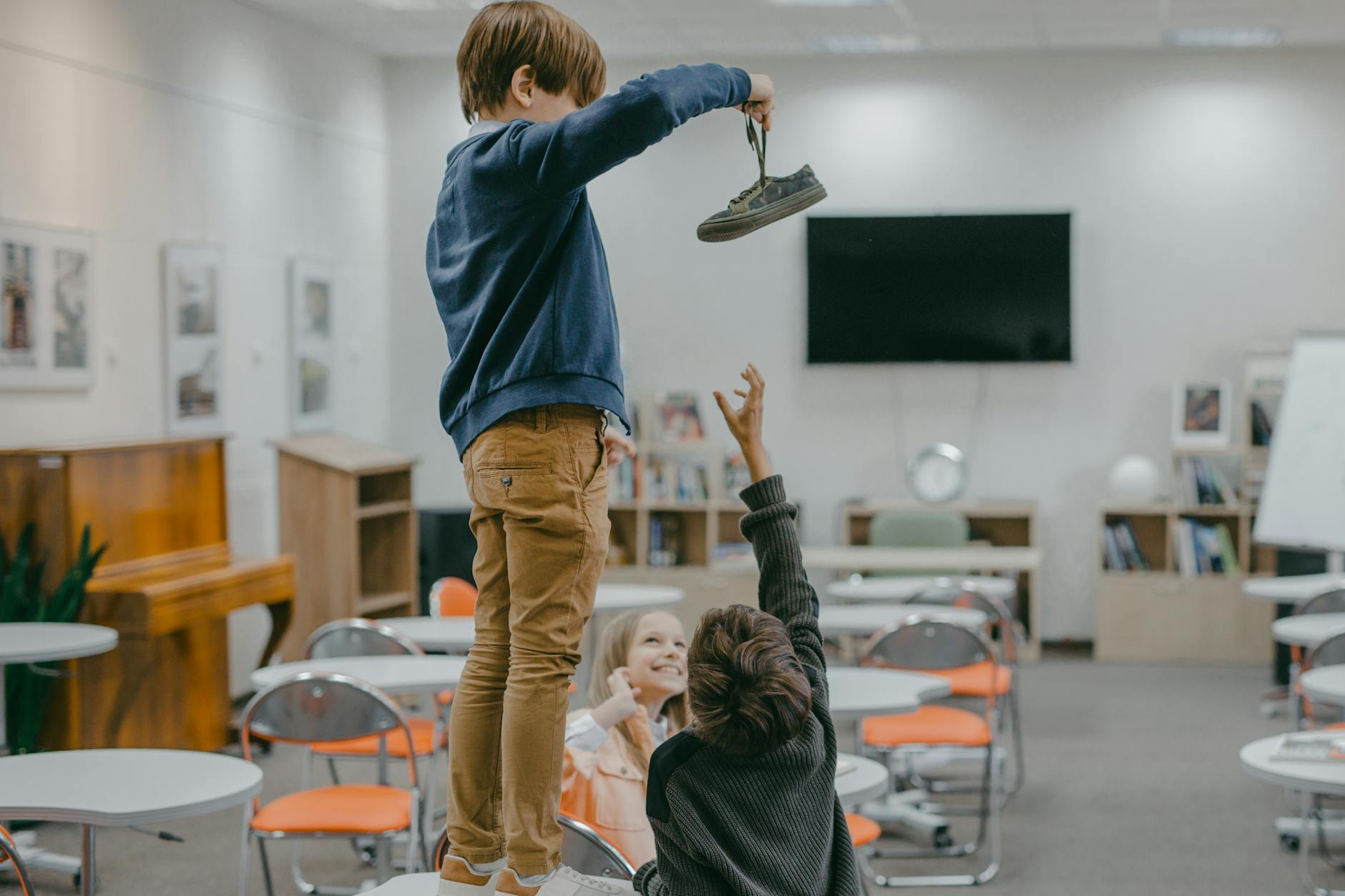 Children interacting in a classroom setting, playfully reaching for an object.