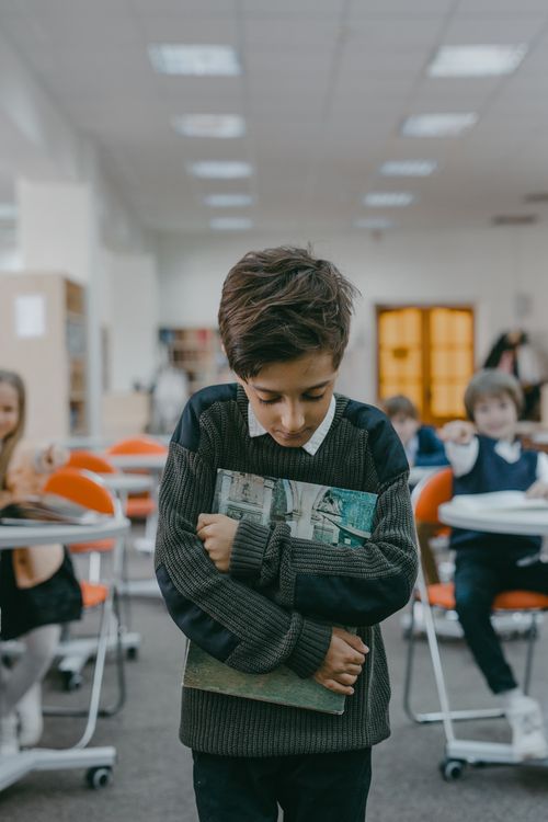 Free Sad boy holding books tightly, showing signs of bullying and isolation in a classroom. Stock Photo