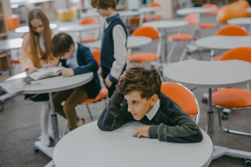 Free A young child feeling left out in a school classroom surrounded by peers. Stock Photo
