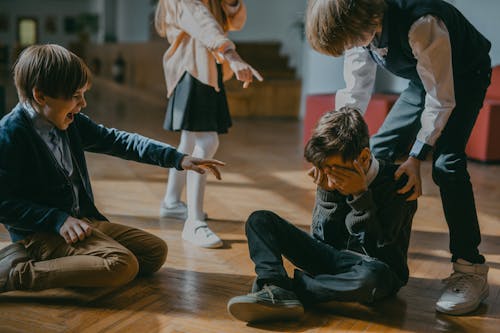 Free Children Finger Pointing at a Boy Sitting on a Wooden Floor Stock Photo