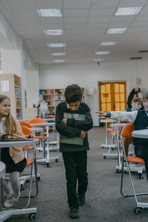 Free A sad child walks alone in a classroom, facing bullying from classmates. Stock Photo