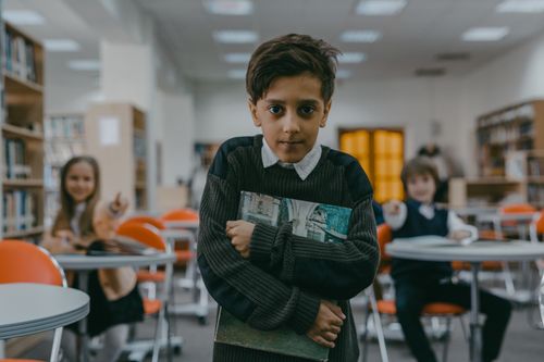 Free Young boy in school library looking sad while classmates point and laugh. Stock Photo