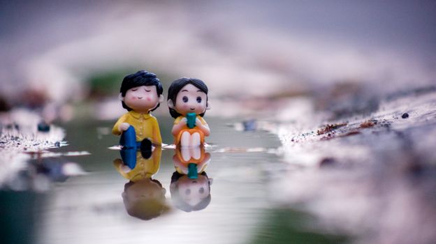 Close-up of two adorable figurines sitting by a water reflection, evoking romance and serenity.