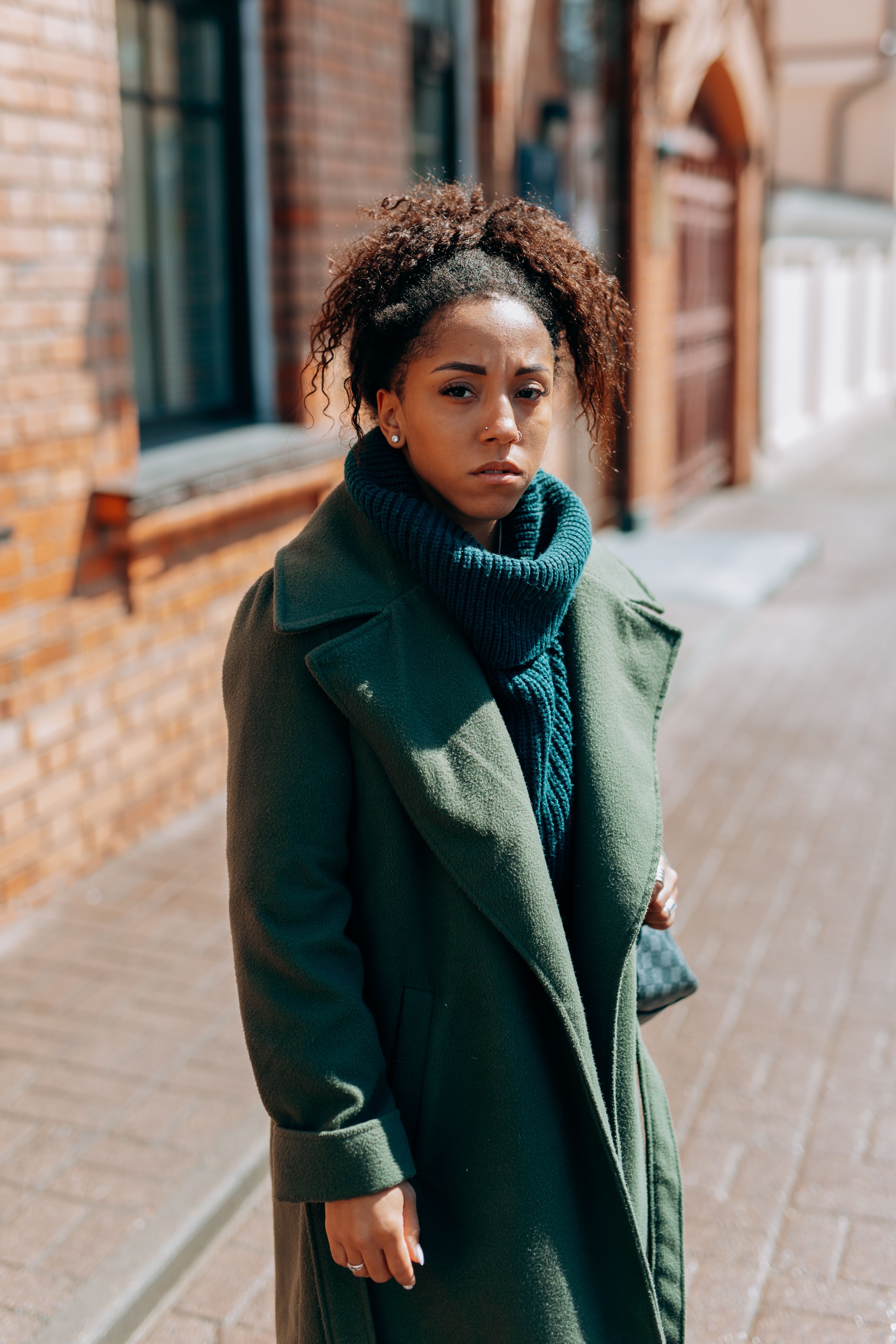 Woman in Green Coat Sitting and Leaning on a Brick Wall · Free Stock Photo