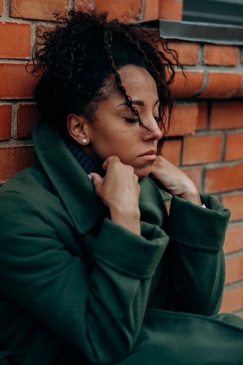 Free Woman in Green Coat Sitting and Leaning on a Brick Wall Stock Photo