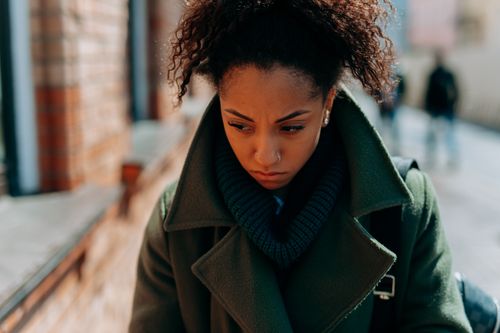 Free A young woman in a trench coat appears thoughtful and pensive walking down a city street. Stock Photo