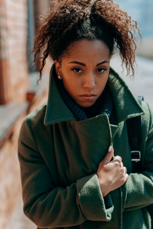 Free A young woman with curly hair and nose ring in green coat. Outdoors, urban setting. Stock Photo