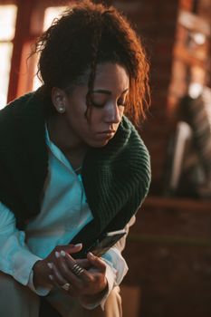 A woman with curly hair sits thoughtfully indoors, wearing a green sweater.