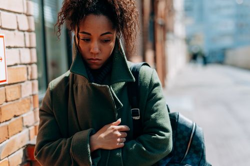 Free Thoughtful woman in a coat walking down a city street in daylight. Stock Photo