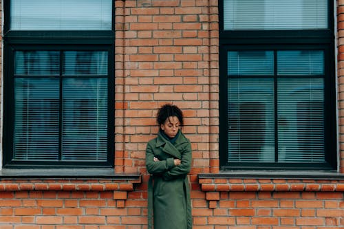 Woman in Green Coat Leaning on a Brick Wall