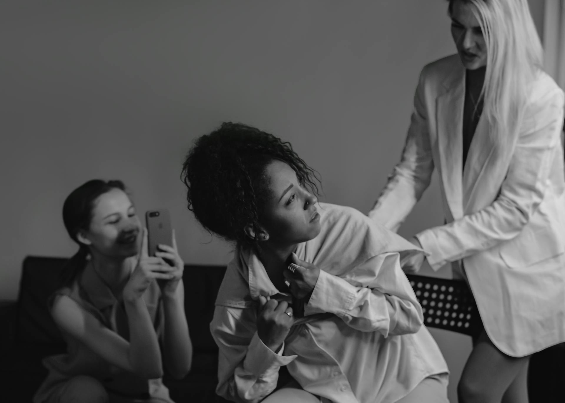 Photo en gris d'une femme en blazer blanc qui harcèle une femme en chemise blanche