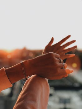 Close-up of hands adorned with rings and bracelets against a sunset backdrop, showcasing elegance and style.
