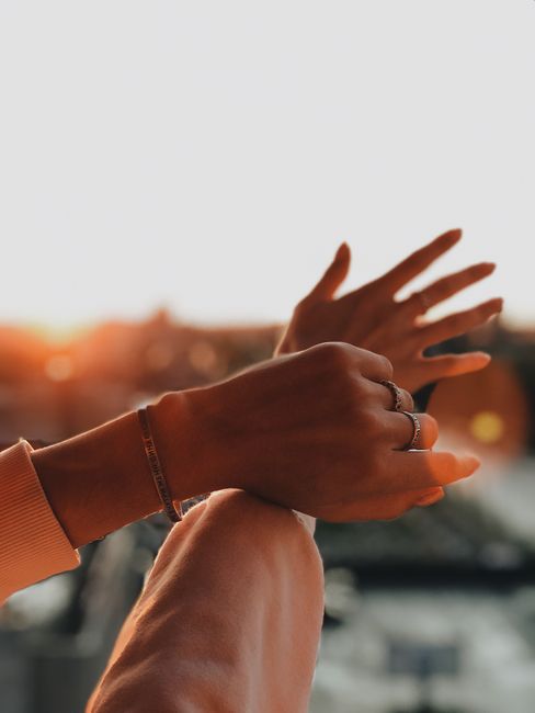 Close-up of hands adorned with rings and bracelets against a sunset backdrop, showcasing elegance and style.