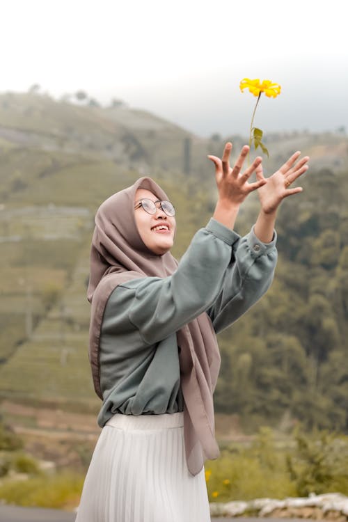 Free Woman Wearing a Headscarf and Green Long Sleeves Catching a Flower Stock Photo