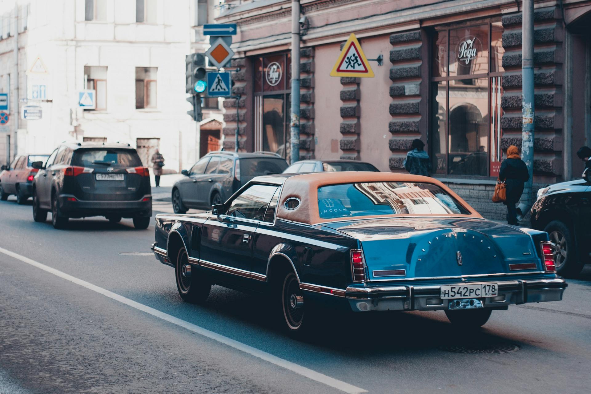 Vintage Lincoln Continental driving down a bustling urban street with classic architecture in the background.