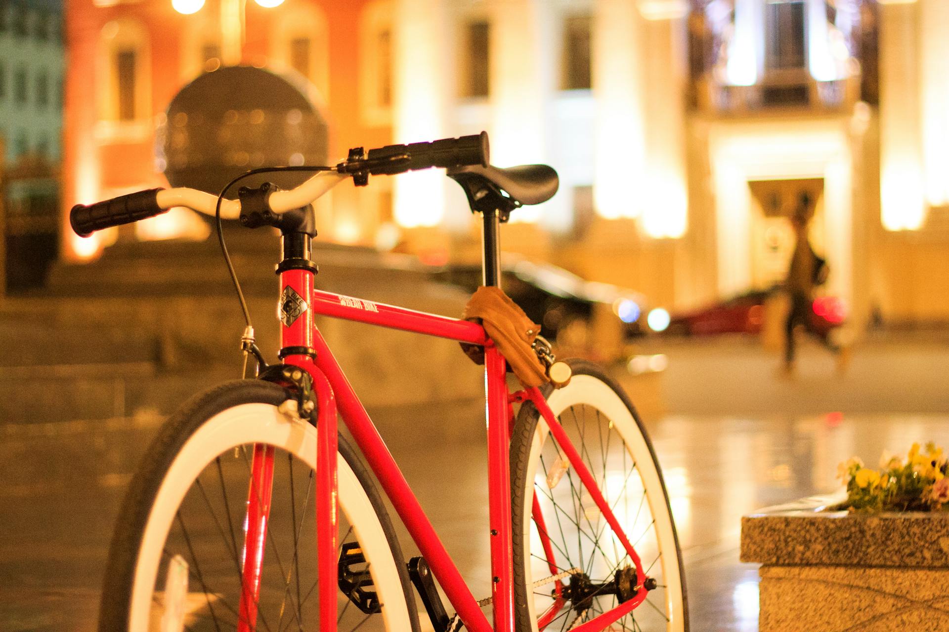 A stylish red bike secured in an urban setting, captured during the evening with blurred lights.