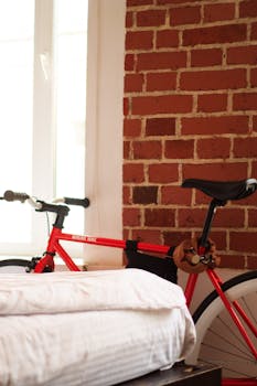 A red bicycle parked indoors against a stylish brick wall beside a bed.
