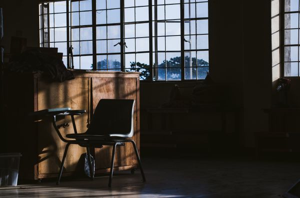 An empty chair in a quiet room lit through tall windows — photo by Nothing Ahead on Pexels