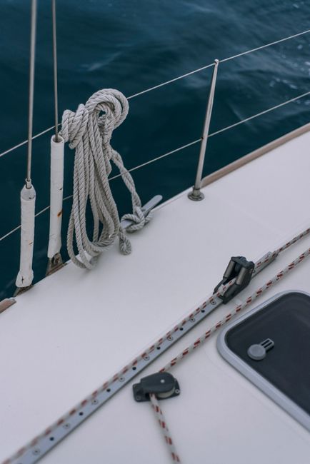 Close-up of sailing yacht deck featuring ropes, metal railing, and ocean view.