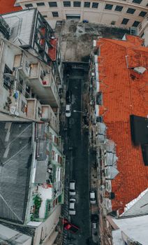 Drone view of narrow asphalt road with cars between shabby residential houses in old district