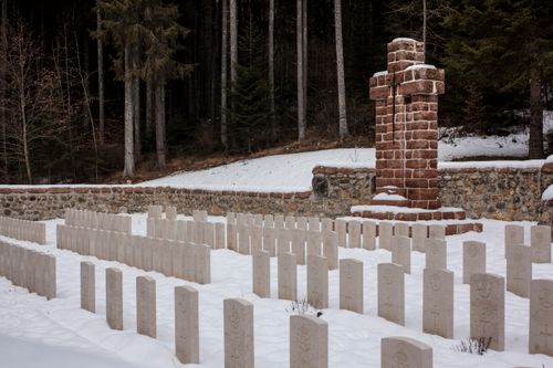 Free A serene winter scene featuring a cemetery with snow-covered tombstones and a prominent red brick cross. Stock Photo