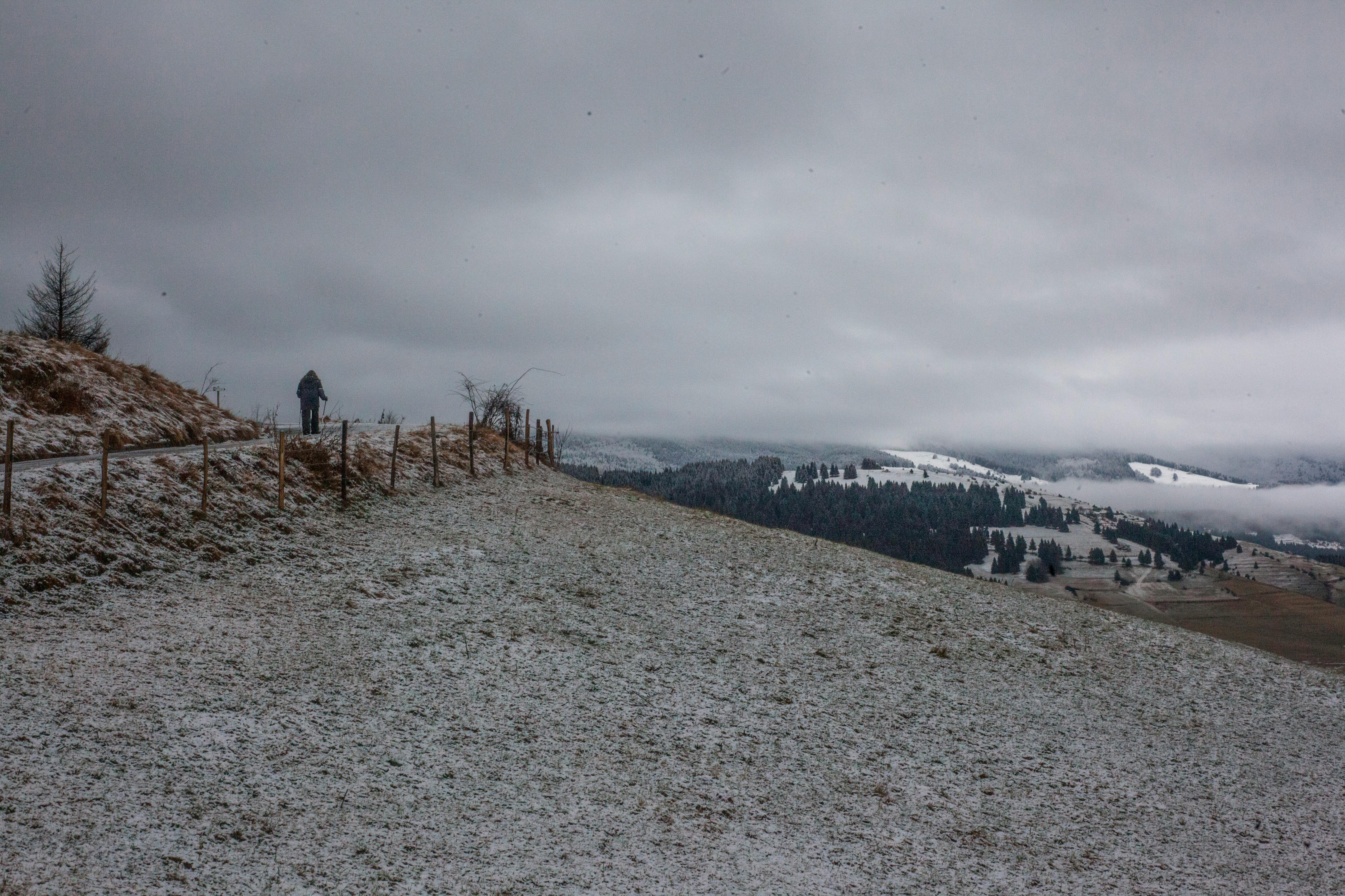 雪道旁，一个孤独的人行走在优美的风景和多云的天空下