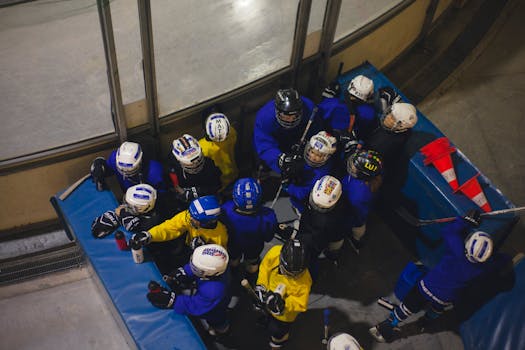 Top view of youth ice hockey team huddling indoors at a rink, wearing helmets and uniforms.