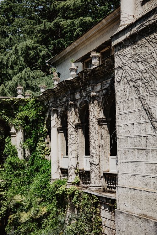 Free A historic stone building with overgrown plants and vines covering its pillars and walls. Stock Photo