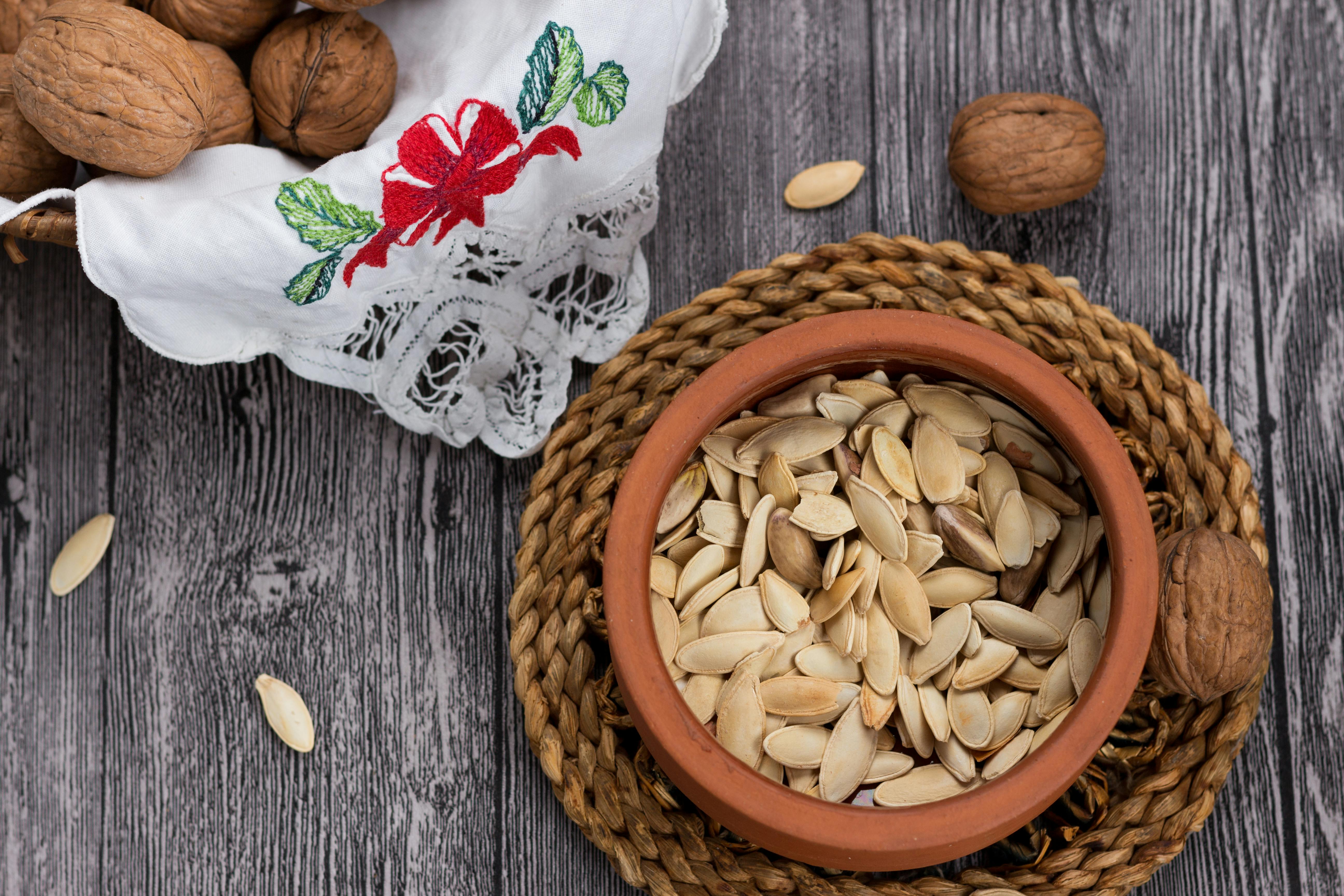 Close-up of pumpkin seeds in a terracotta bowl with walnuts on a rustic wooden surface. Perfect for food photography.