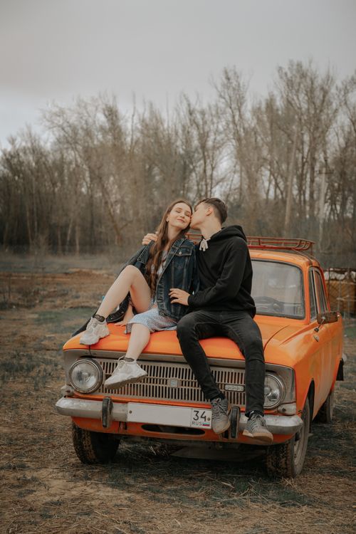 Free Millennial man embracing and kissing smiling female beloved on aged automobile against trees in fall Stock Photo