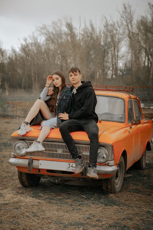 Free Young cool man embracing female beloved touching forehead while looking at camera on old auto in autumn countryside Stock Photo