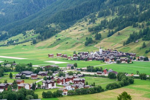 Free A picturesque Swiss village nestled in a lush green valley with rolling hills and quaint houses. Stock Photo