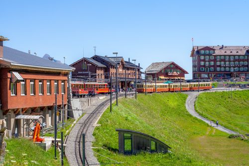 Free Colorful train passes through a picturesque alpine village under a clear blue sky. Stock Photo