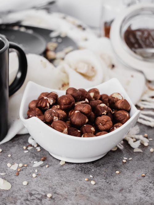 Free Hazelnuts in a White Ceramic Bowl on a Messy Kitchen Table Stock Photo