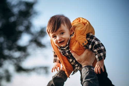 Free From below of crop unrecognizable male holding adorable little boy in warm clothes looking at camera Stock Photo