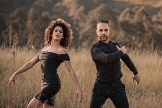 Elegant couple striking a pose in a serene outdoor setting with lush grass and warm tones around.