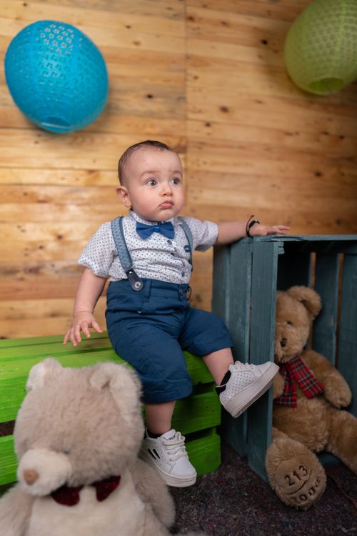 Free Adorable baby boy in stylish outfit surrounded by colorful decor and teddy bears. Stock Photo