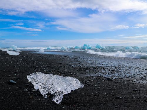 Free Breathtaking view of icebergs on a black sand beach with waves and blue sky. Stock Photo
